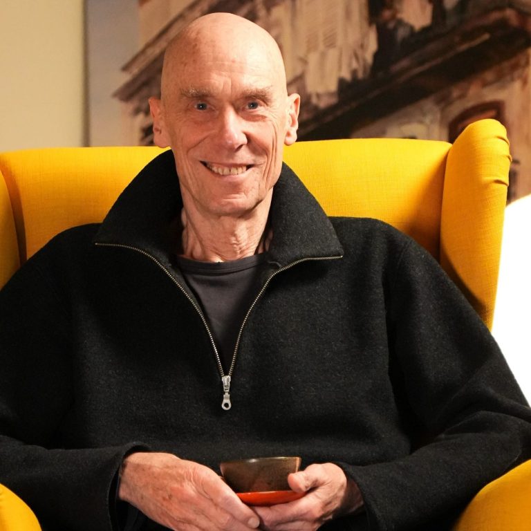 Gerald Weischede sitzt lächelnd in einem gelben Sessel und trinkt Tee aus einer Teeschale.