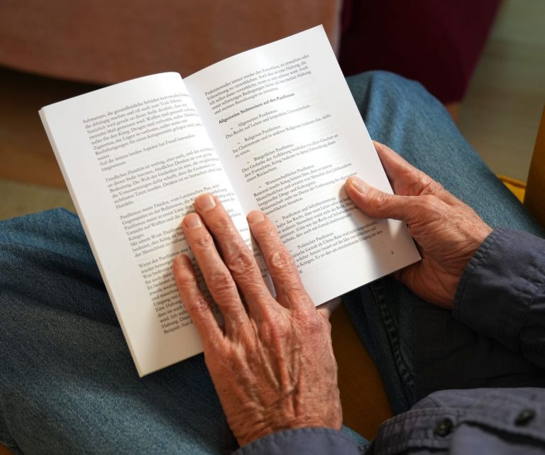Gerald Weischede hält ein Buch in der Hand und man sieht das Buch aufgeschlagen liegen.