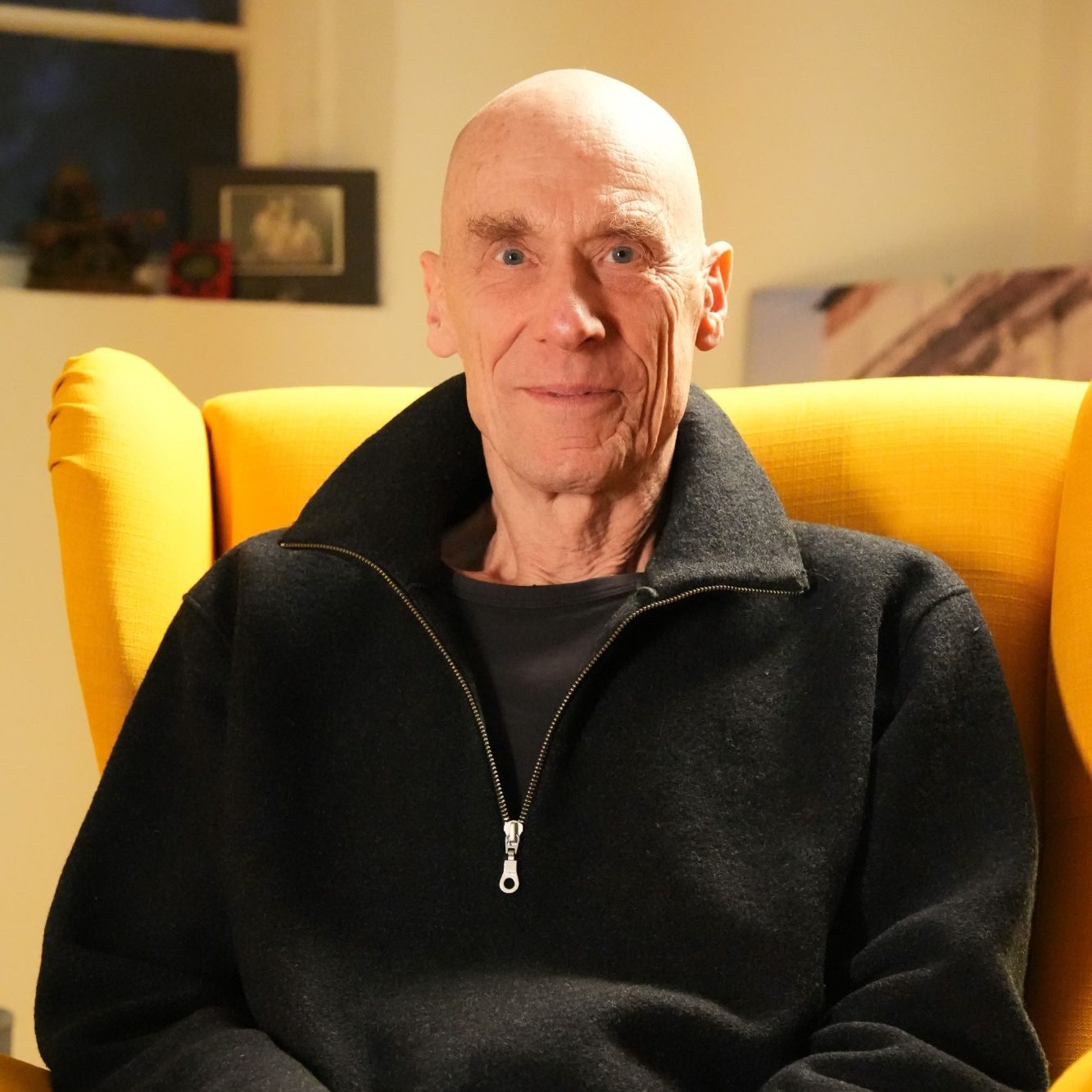Gerald Weischede sitzt lächelnd in einem gelben Sessel.